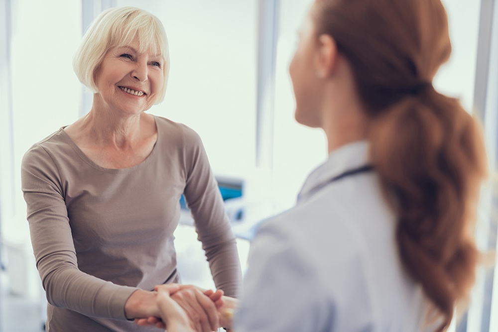 Smiling elderly woman shaking hands with physician after visit to clinic